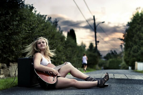 Chica con guitarra sentada en el asfalto