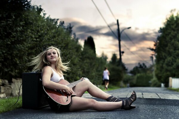 La ragazza con la chitarra si siede sull asfalto