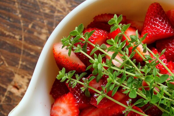 Red strawberries in a saucer with green twigs