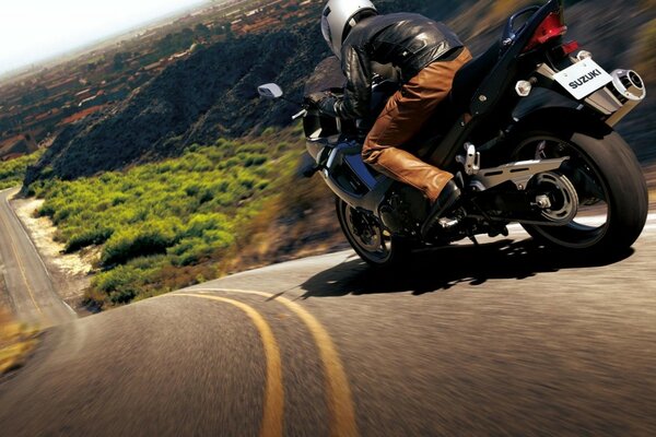 A motorcyclist rides down a hill. The motorcycle is on the road. Nature