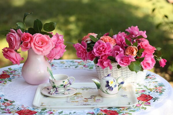 Florero con rosas, taza y Tetera en la mesa