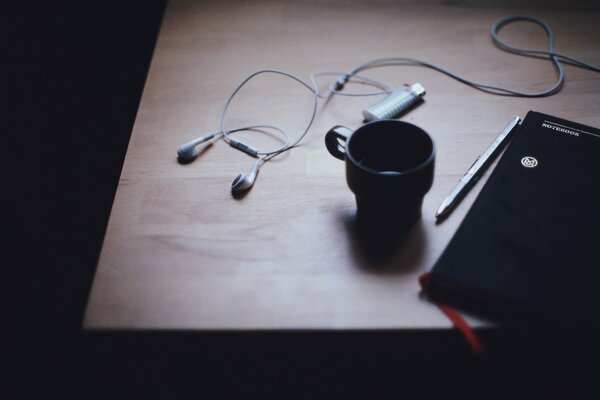 On the table there is a diary a cup and headphones