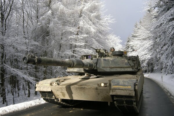 The tank is driving along the road among the snow-covered forest