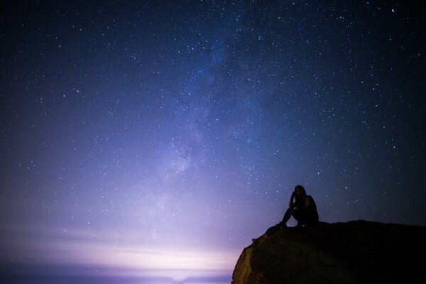 Mädchen auf einem Felsen in der Nacht vor dem Hintergrund des Sternenhimmels