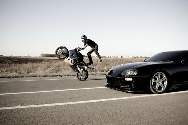 A motorcyclist performs a stunt on the road next to a car