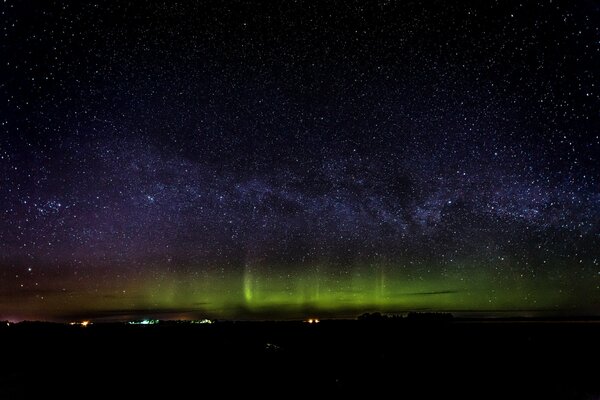 Aurora boreale, terra oscura, luci della città e cielo stellato