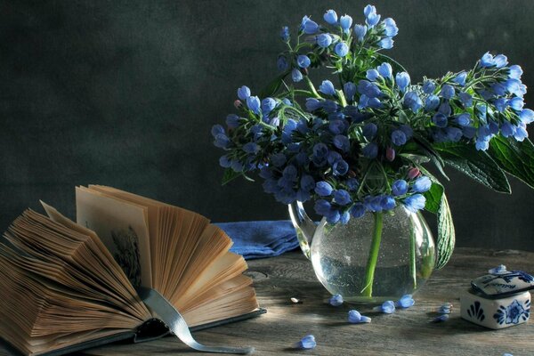 Natura morta di fiori blu in un vaso con un antico libro