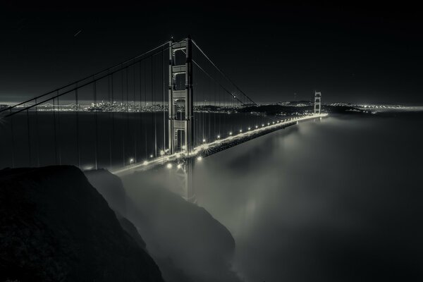 Puente de la bahía de la noche en la niebla. Luces de la ciudad nocturna