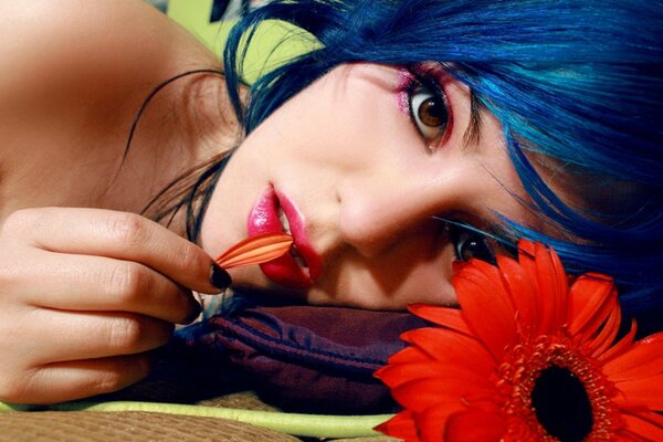 A model with blue hair poses next to a flower