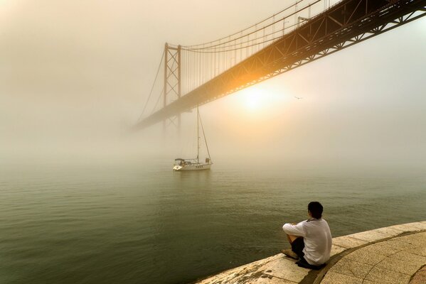 Mężczyzna patrzy na wschód słońca nad mgłą i mostem