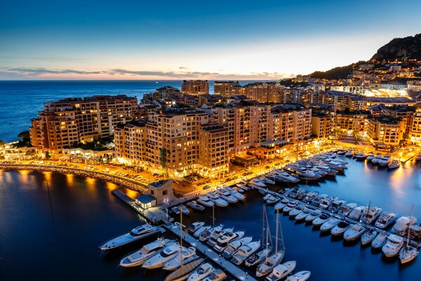 Fonway, Principado de Mónaco. Ciudad de la noche en la costa azul, rodeada de agua, en el fondo de las montañas
