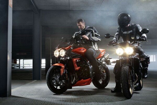 Two people are sitting on motorcycles in the parking lot