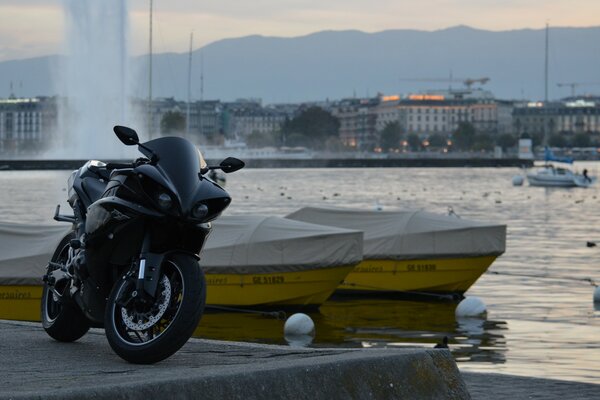 Black Yamaha motorcycle on the embankment. Fountain. Boats at the pier