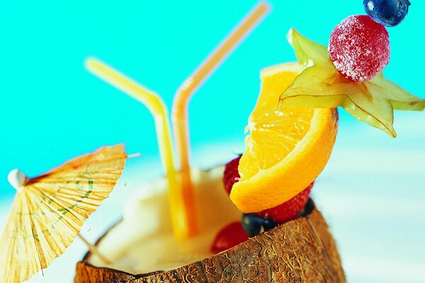 Tropical cocktail in coconut with umbrella and fruit on a skewer