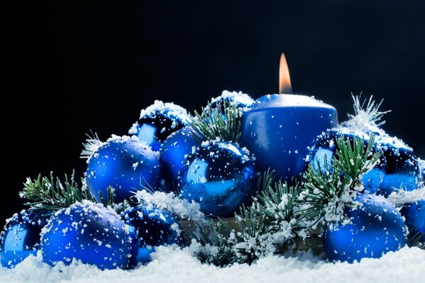 Vela ardiente en la nieve con juguetes de Navidad