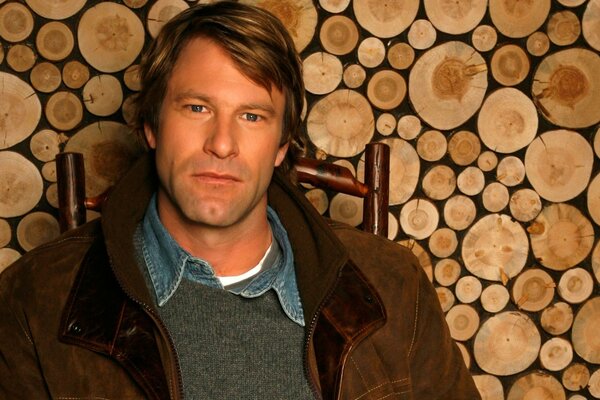 Aaron Eckhart su una sedia in giacca marrone