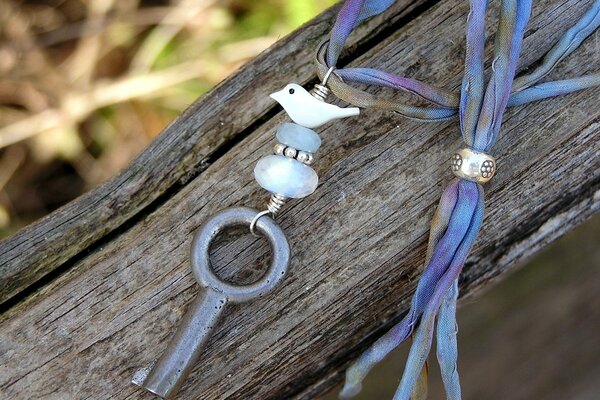 Pendant with a bird and a key on the background of a tree trunk