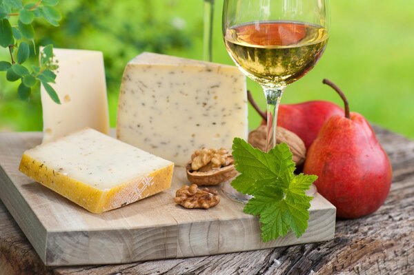 Queso en una tabla de cortar con vino blanco y peras