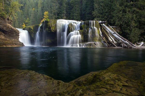 Wasserfall umgeben von dunkelgrünen Wäldern und Flusslandschaft