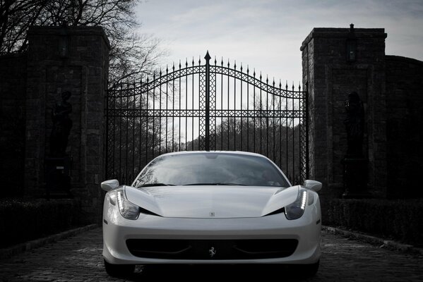 A white Ferrari stands in front of a wrought-iron gate