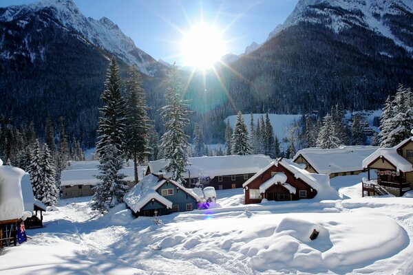 Зимняя деревня окутанная снегом на фоне яркого солнца