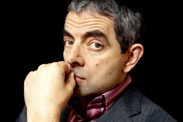 Rowan Atkinson holds his hand near his mouth