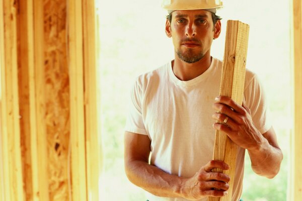 Un maestro constructor con un casco sostiene una tabla