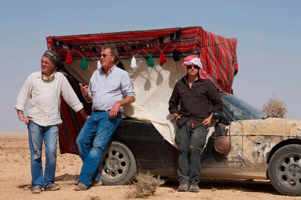 Tres hombres de pie junto a un coche en el desierto