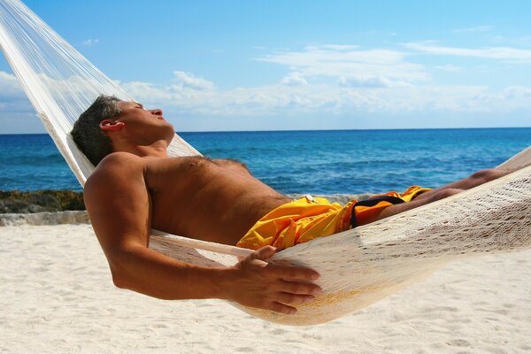 A man is resting in a hammock on the seashore