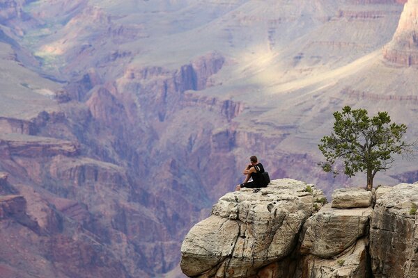 A man is sitting on a cliff in a beautiful canyon