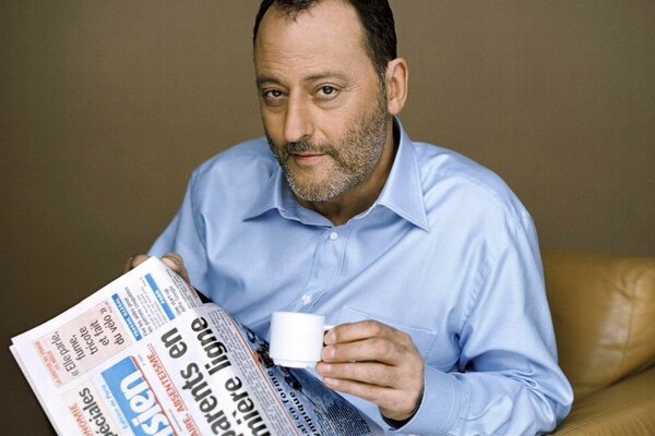French actor Jean Renaud reads a newspaper with a cup of coffee