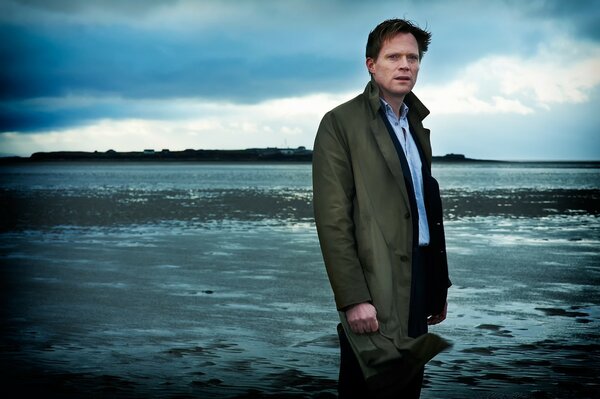 A man stands on the seashore in a raincoat