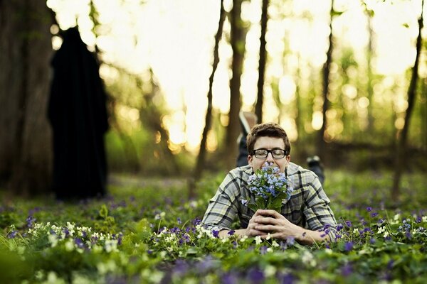 A man is lying in a clearing in the forest with a bouquet of flowers