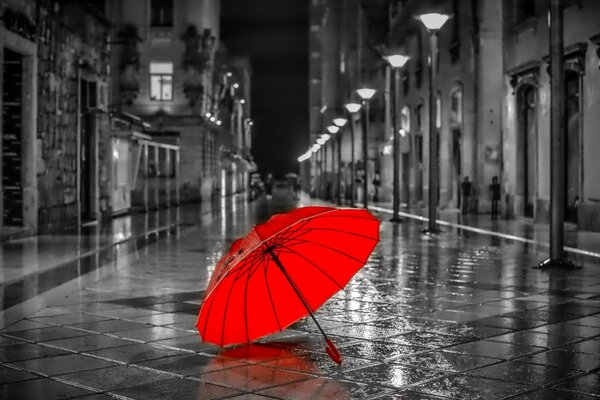 A bright red umbrella lies on the asphalt wet from the rain among the gray alley of the night city