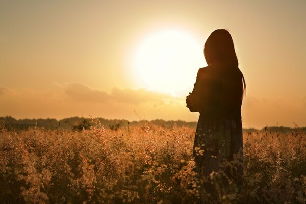 Chica solitaria en el fondo de la puesta de sol y las flores