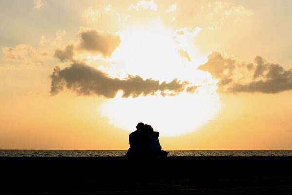 Una pareja abrazada se sienta en medio de una puesta de sol en el mar