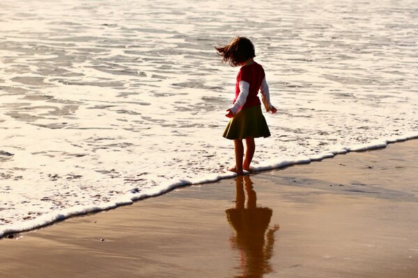 Girl wets her feet in the water on the beach