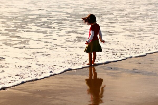 Девочка мочит ноги в воде на пляже