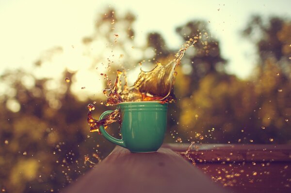 Spritzender Kaffee im grünen Becher vor dem Hintergrund der Natur