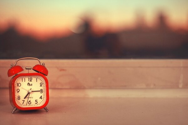Red alarm clock on the background of a blurred city