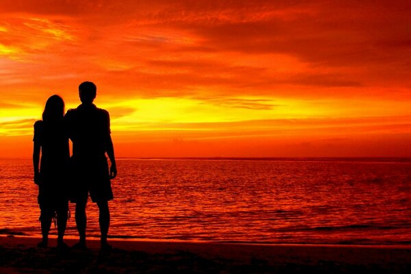 Uomo e donna in piedi sulla riva al tramonto