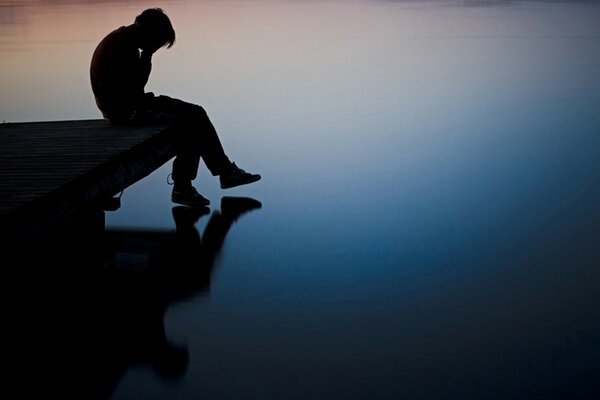 A boy sitting on a pier by the river is pining