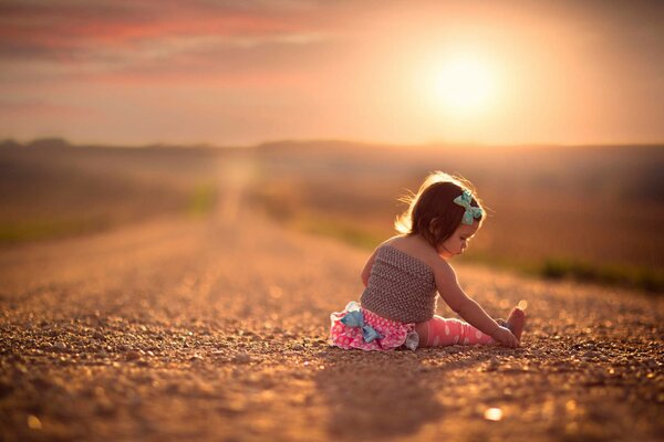 Petite fille assise sur la route dans la lumière du coucher du soleil