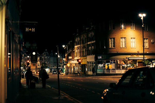 Personas caminando por la acera y pasando junto a los coches en la carretera en Londres bajo la luz de la noche