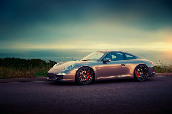 A shiny Porsche stands on a smooth road against the background of the sea going over the horizon