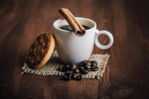 Auf einem Holztisch eine weiße Tasse Kaffee, Zimt, Leber und Kaffeebohnen