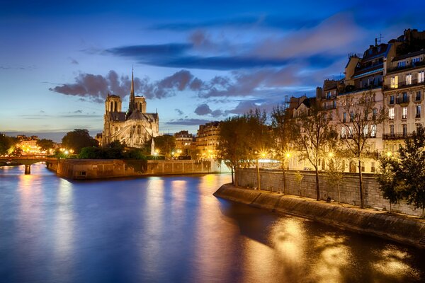 Notre Dame de Paris on the water with lights on the background of the evening cloudy sky