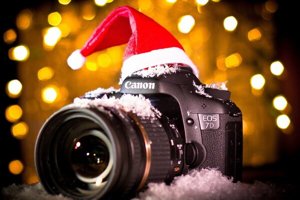 Appareil photo dans le chapeau et la neige sur fond de guirlandes lumineuses