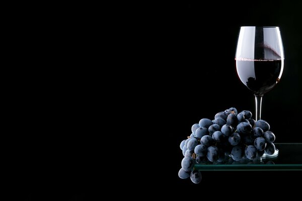 Red wine with a bunch of grapes on a black background