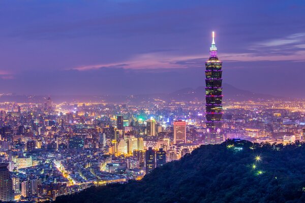 Una torre alta en una ciudad China detrás de colinas verdes en los colores de una puesta de sol púrpura